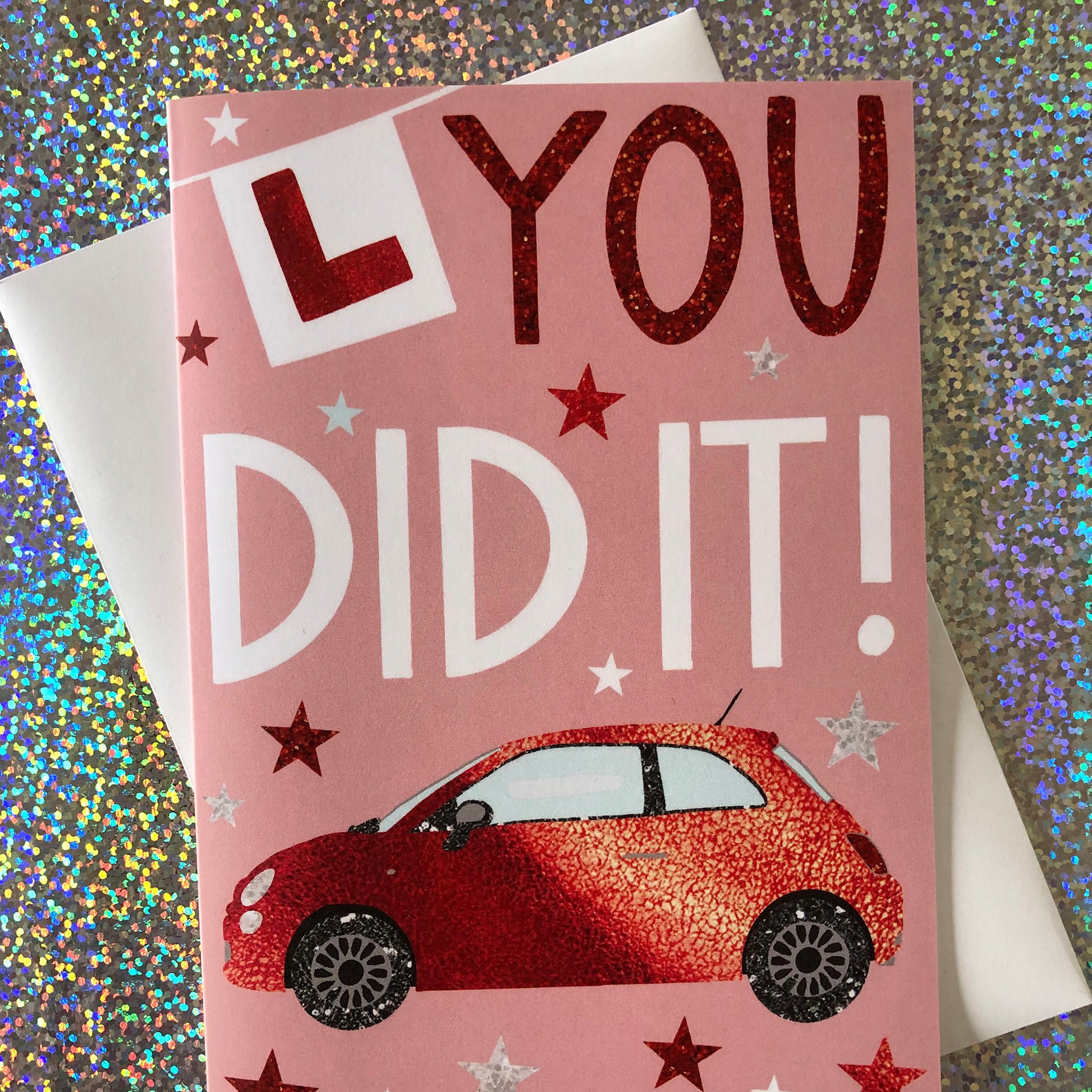 Image shows a pastel pink card with a red sparkly car and L Plate with the words "You Did It!'