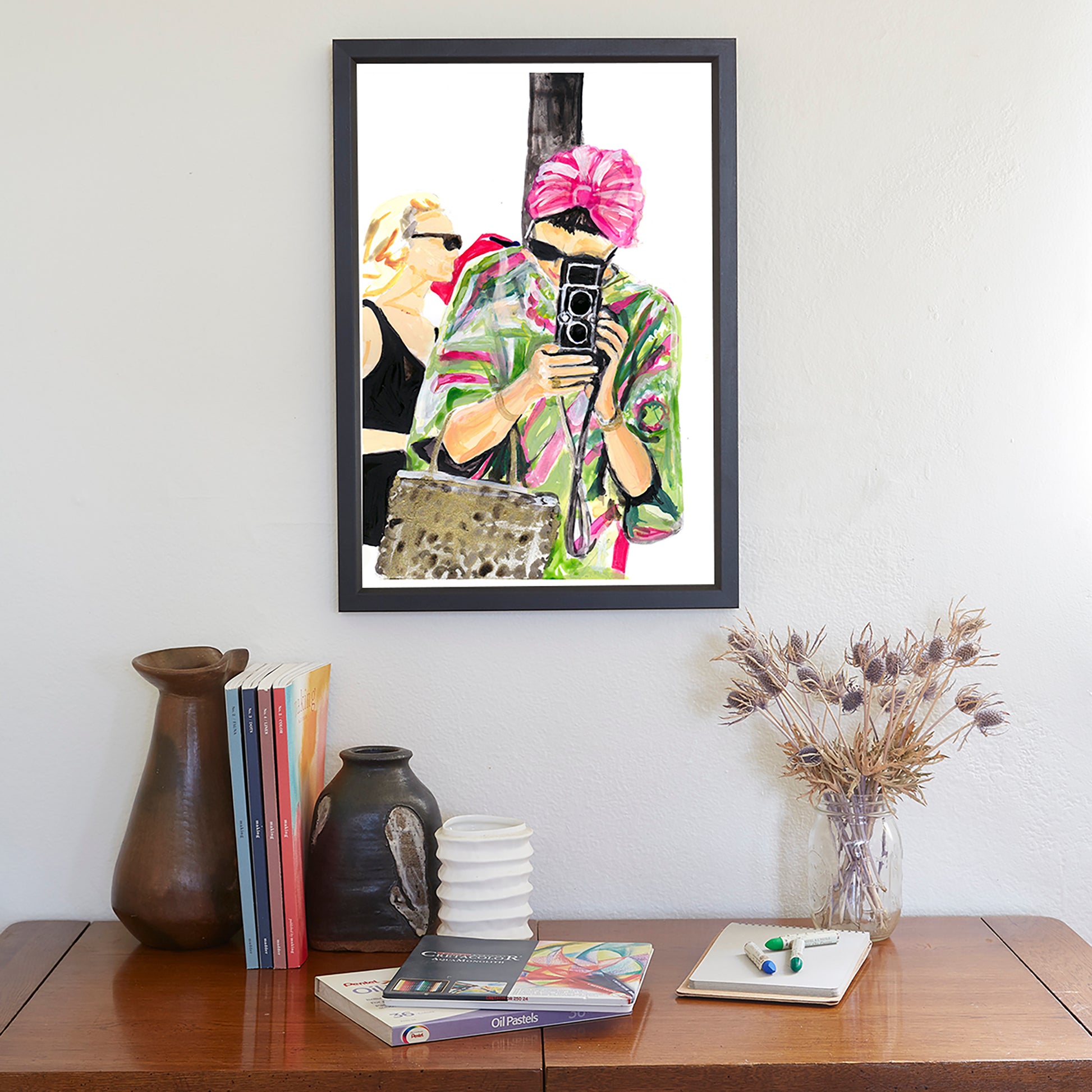 Image shows an illustration of a woman in a pink and green kaftan, black sunglasses and pink turban holding a vintage camera.