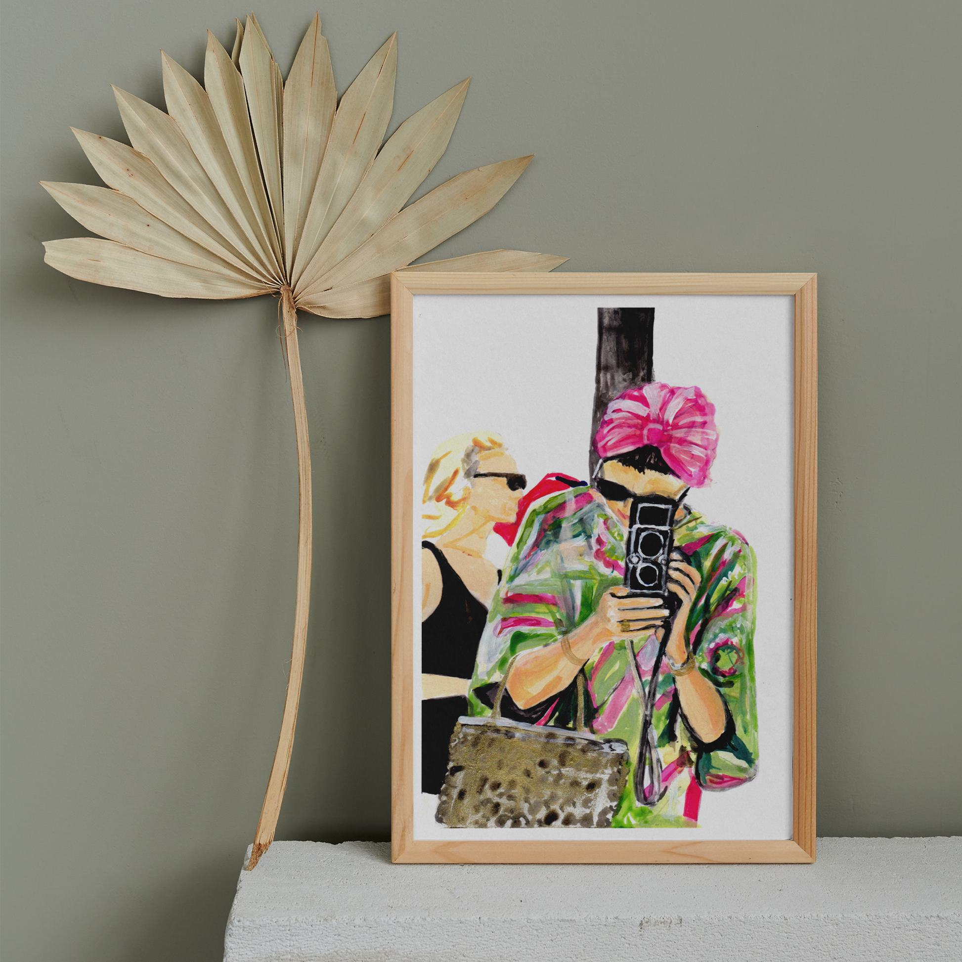 Image shows an illustration of a woman in a pink and green kaftan, black sunglasses and pink turban holding a vintage camera.