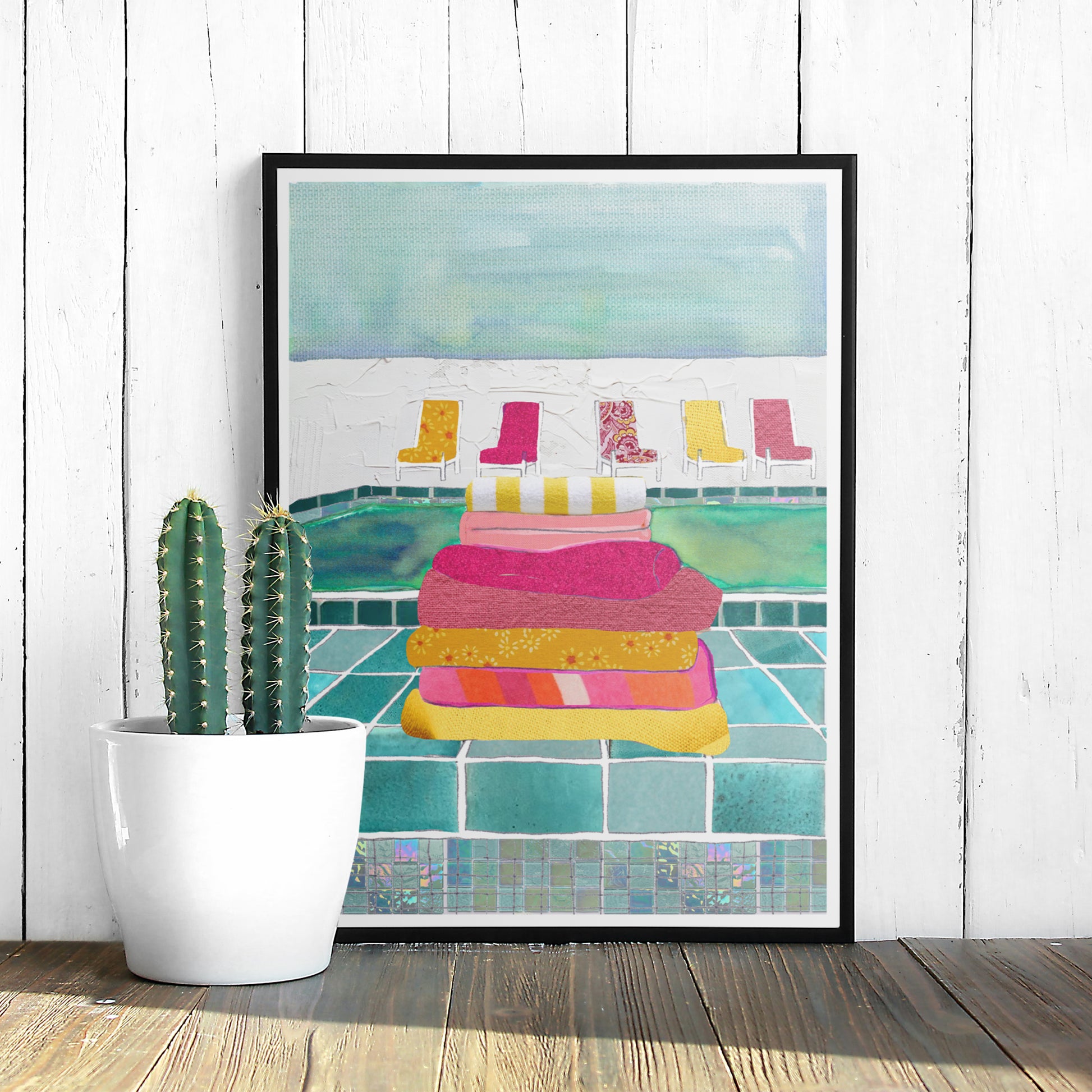 Framed illustration of a poolside featuring a stack of colourful towels and some chairs.