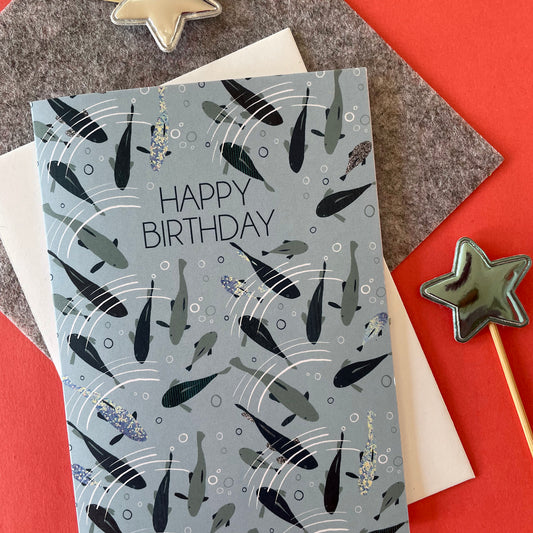 Image shows a pale blue birthday card with blue, silver and grey fish swimming under ripples of water and the words 'Happy Birthday"