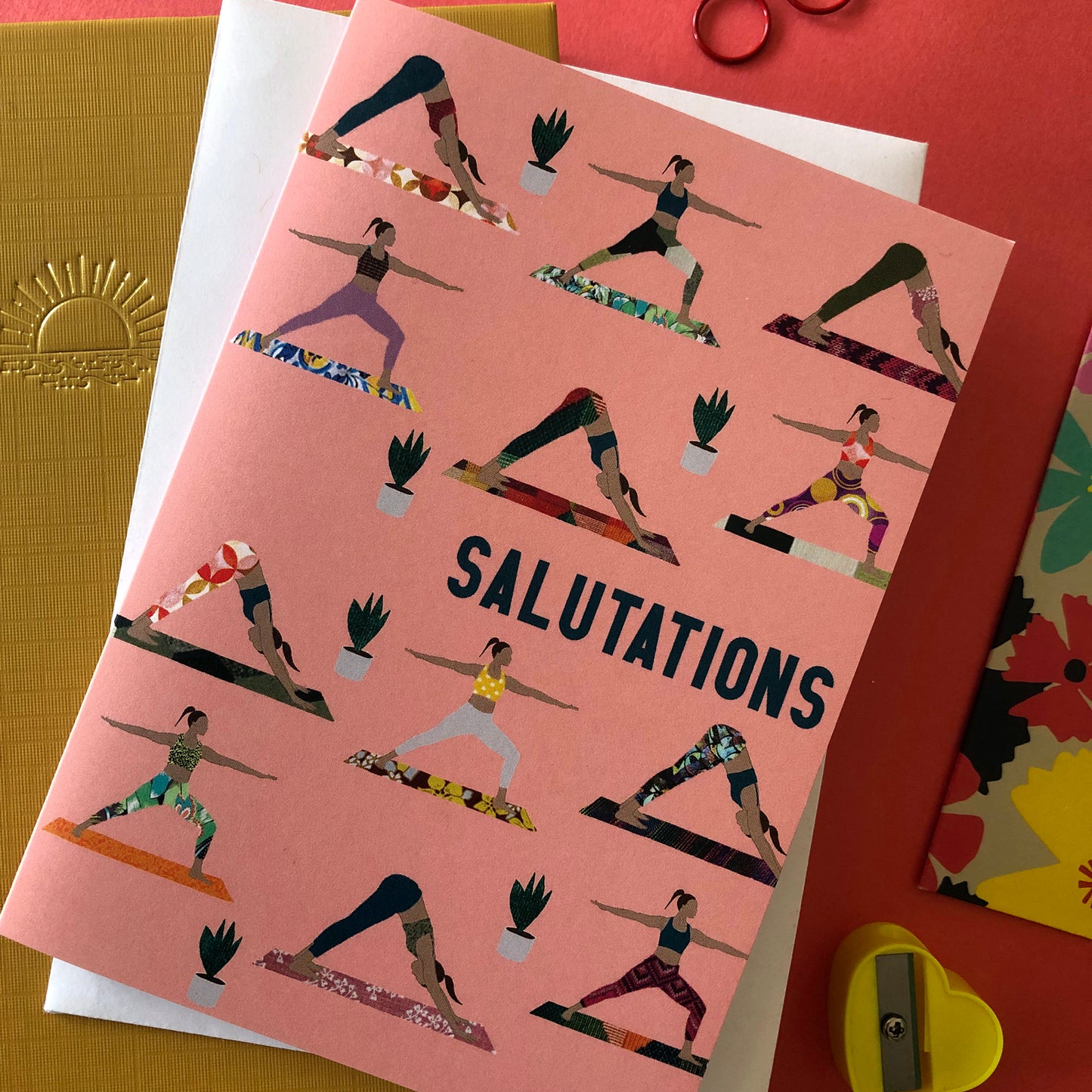 Image shows an everyday greetings card that says 'salutations' and features a fun pattern of women doing yoga poses on colourful yoga mats