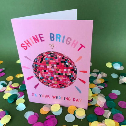 Image shows a pink wedding card featuring a glittery rainbow disco ball illustration and the words 'Shine Bright on your wedding day'.