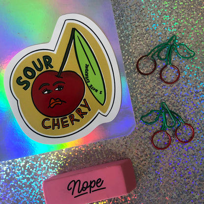 Image shows a vinyl sticker featuring an illustration of an unhappy looking cherry and the wording 'Sour Cherry'