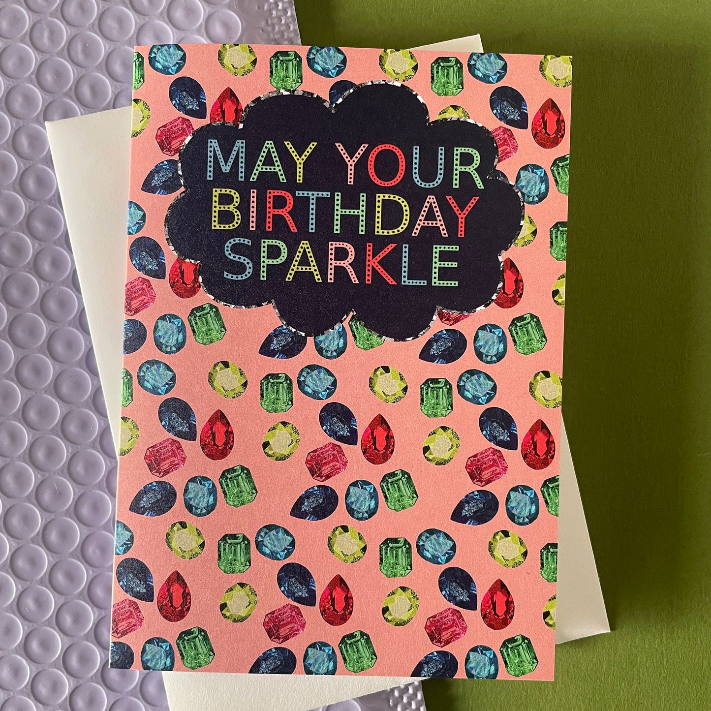 Image shows a sparkly gemstone patterned greetings card with the words may your birthday sparkle.