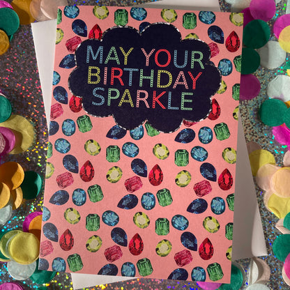 Image shows a sparkly gemstone patterned greetings card with the words may your birthday sparkle.