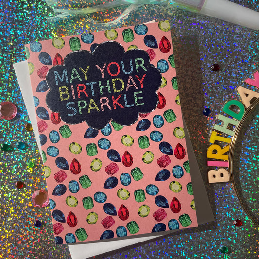 Image shows a sparkly gemstone patterned greetings card with the words may your birthday sparkle.