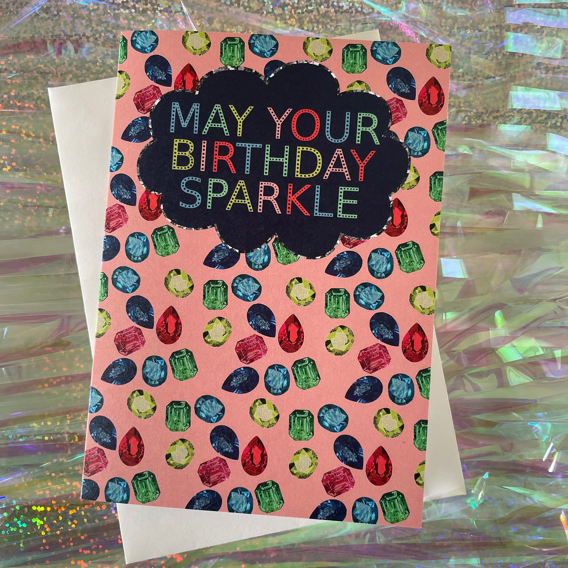 Image shows a sparkly gemstone patterned greetings card with the words may your birthday sparkle.