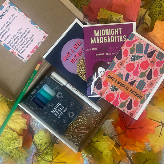 Image shows a seasonal stationery and birthday box with brightly coloured cards, magic spell candles, moon shaped paperclips, glitter marker and basic witch vibes pencil