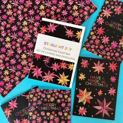 A flat-lay of a 'Starlight Joy' Christmas card set featuring multiple black cards and envelopes decorated with colourful pink, gold, and red star patterns, arranged on a bright turquoise background.