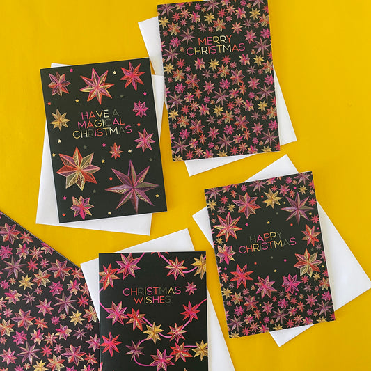 Image shows the 4 different designs of the Starlight Joy Christmas card collection. Each card is black with a hand illustrated, folk art style star pattern.