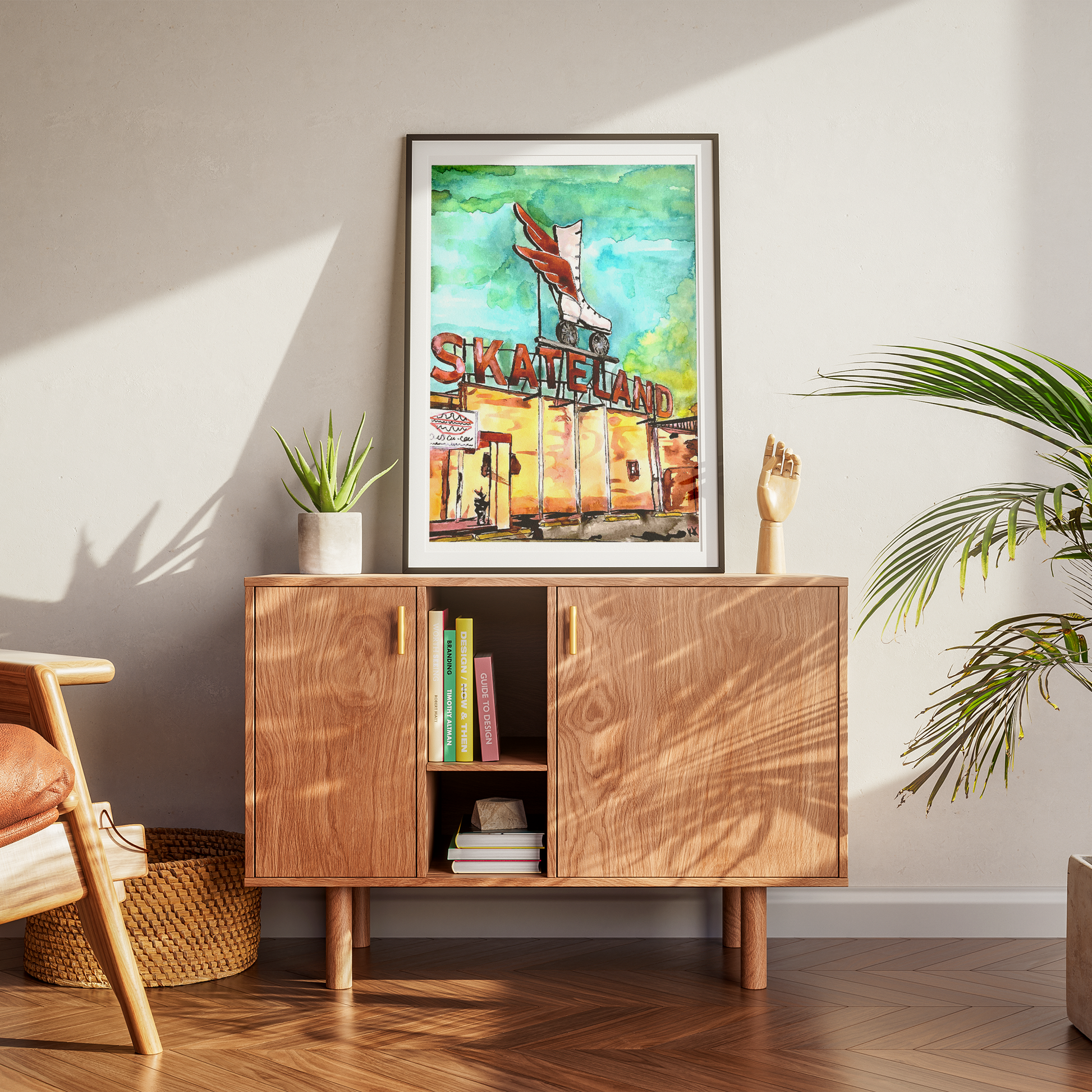 Wooden sideboard with books and a framed picture of 'Skateland' in a room with plants and a chair.