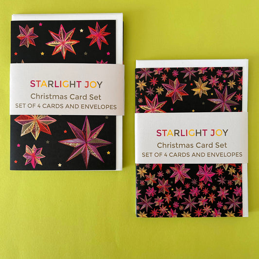 Two copies of the Starlight Joy Christmas Card Set displayed side-by-side on a bright yellow-green background. The set features black cards decorated with colourful starburst patterns in pink, red, and gold, complete with matching envelopes.