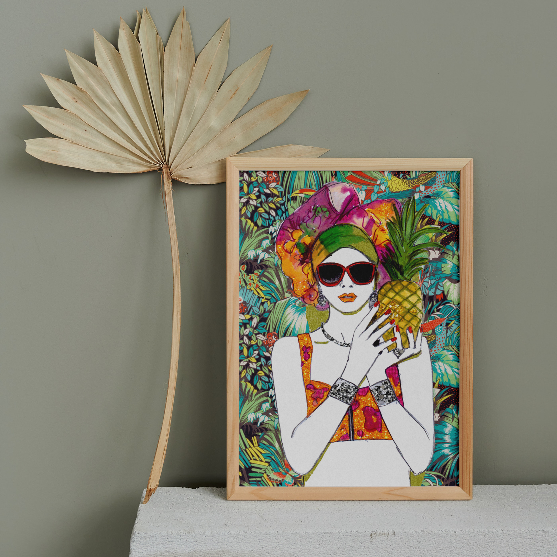 Image shows a framed illustration of a woman holding a pineapple with a colourful head wrap and a bright, tropical, collage background