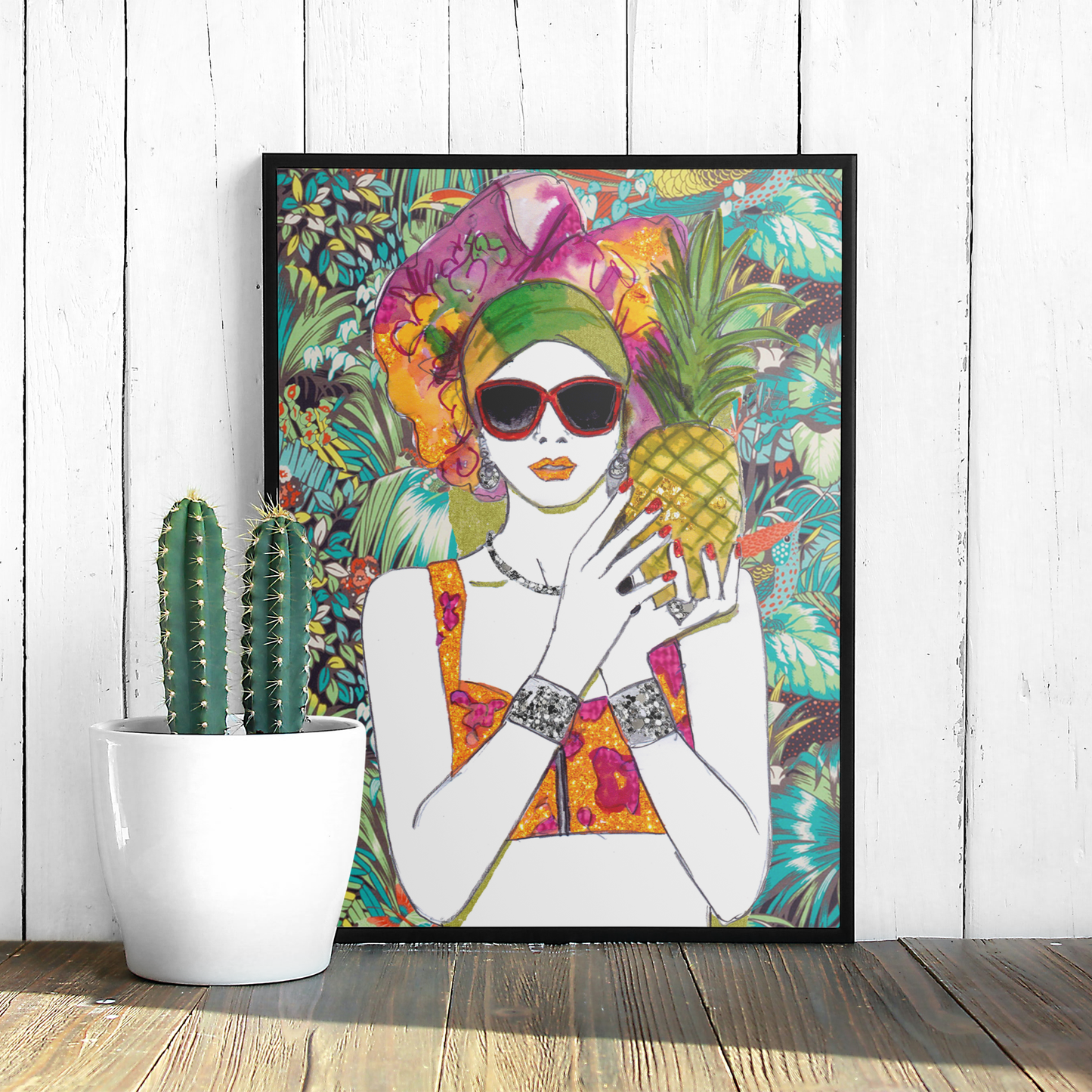 Image shows a framed illustration of a woman holding a pineapple with a colourful head wrap and a bright, tropical, collage background