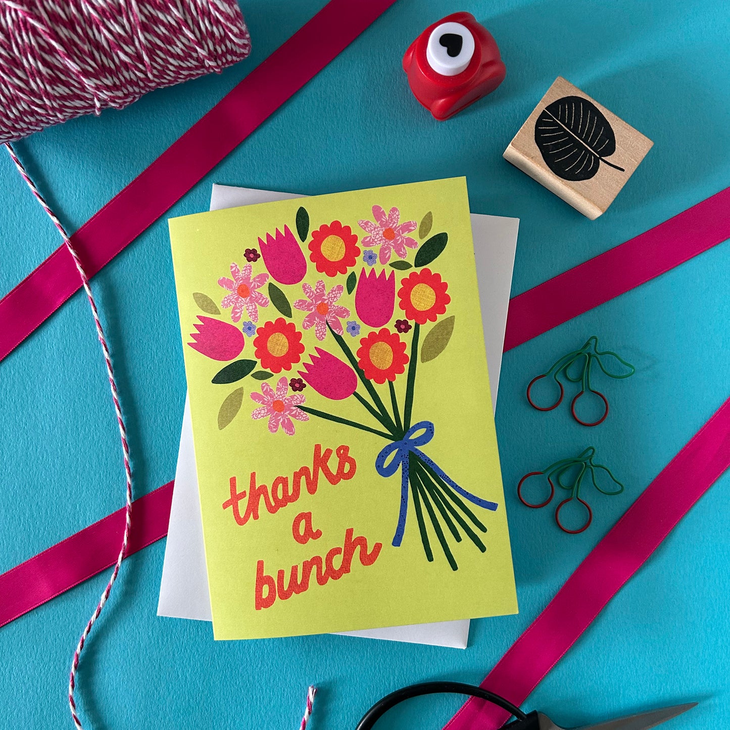 Greeting card with floral design and 'thanks a bunch' text on a blue background with ribbons and stamps.
