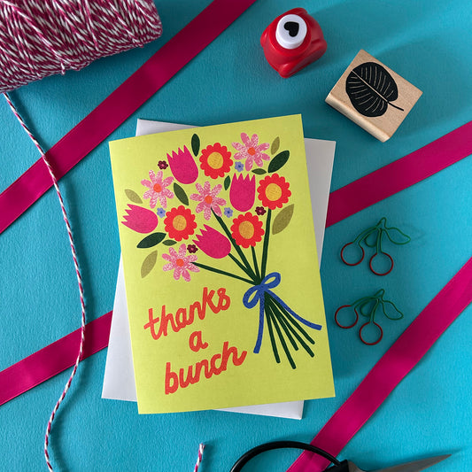 Greeting card with floral design and 'thanks a bunch' text on a blue background with ribbons and stamps.