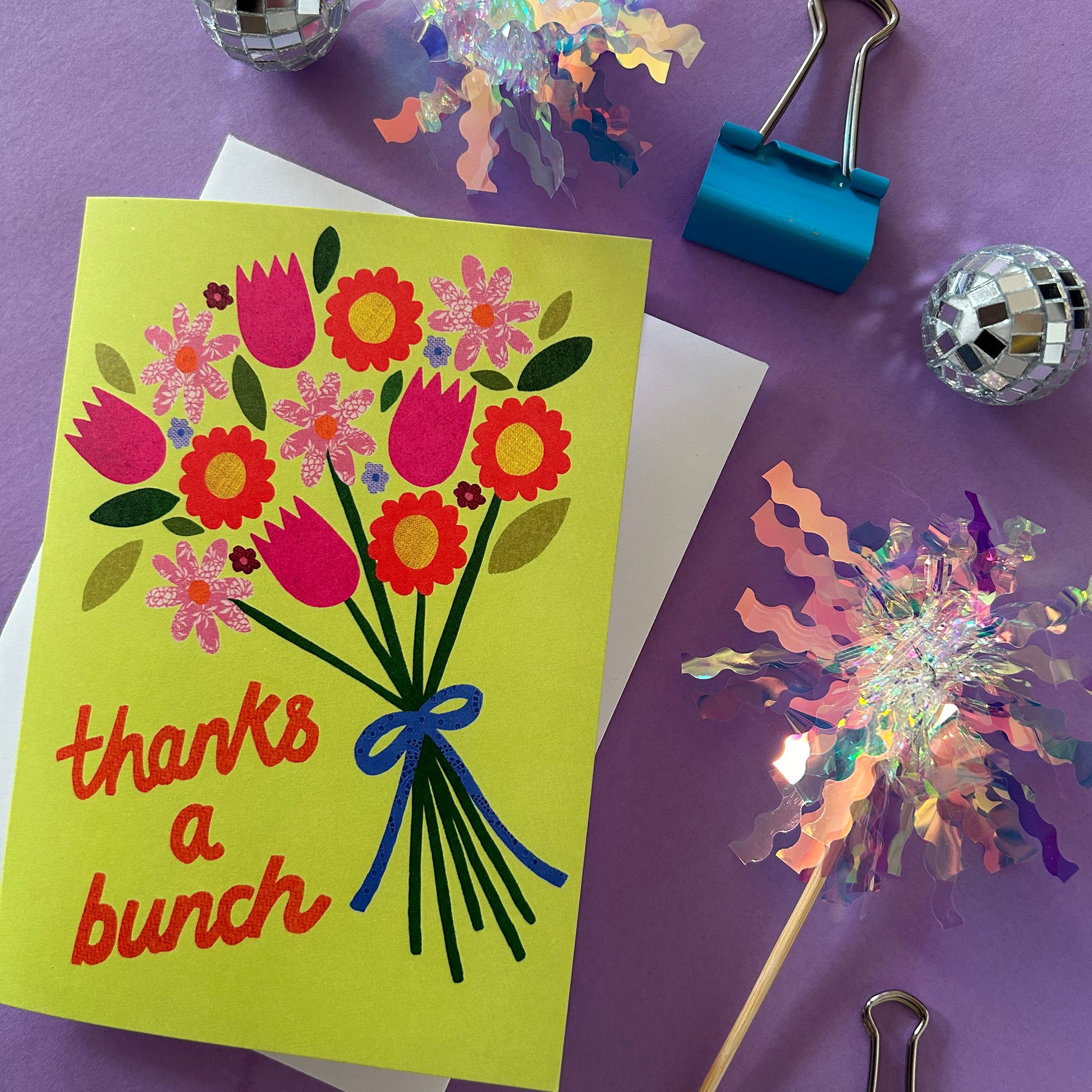Colourful card with flowers and 'thanks a bunch' text on a purple surface with decorative items.