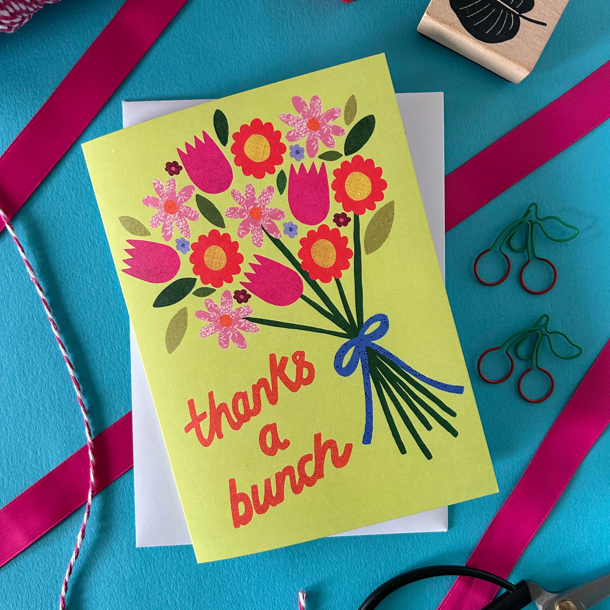 Greeting card with floral design and 'thanks a bunch' text on a blue background with ribbons and stamps.