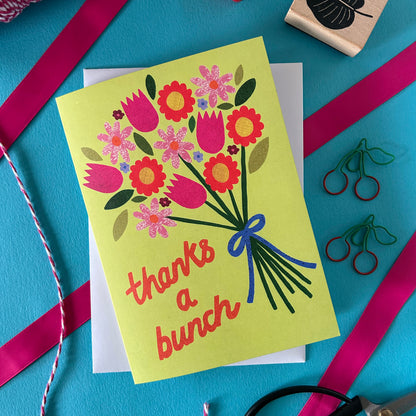 Greeting card with floral design and 'thanks a bunch' text on a blue background with ribbons and stamps.