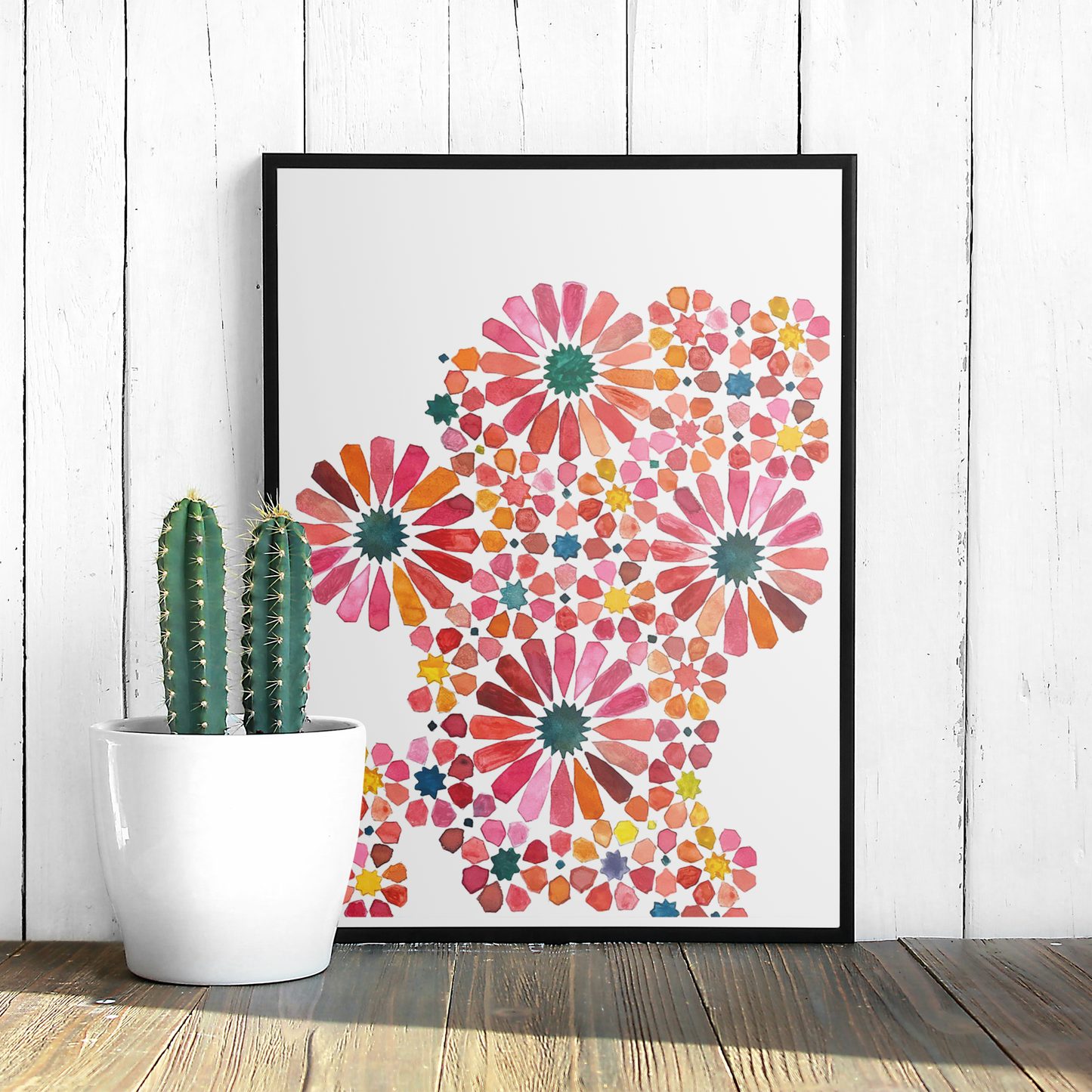 Framed colourful floral art print on a white wall with a cactus plant.
