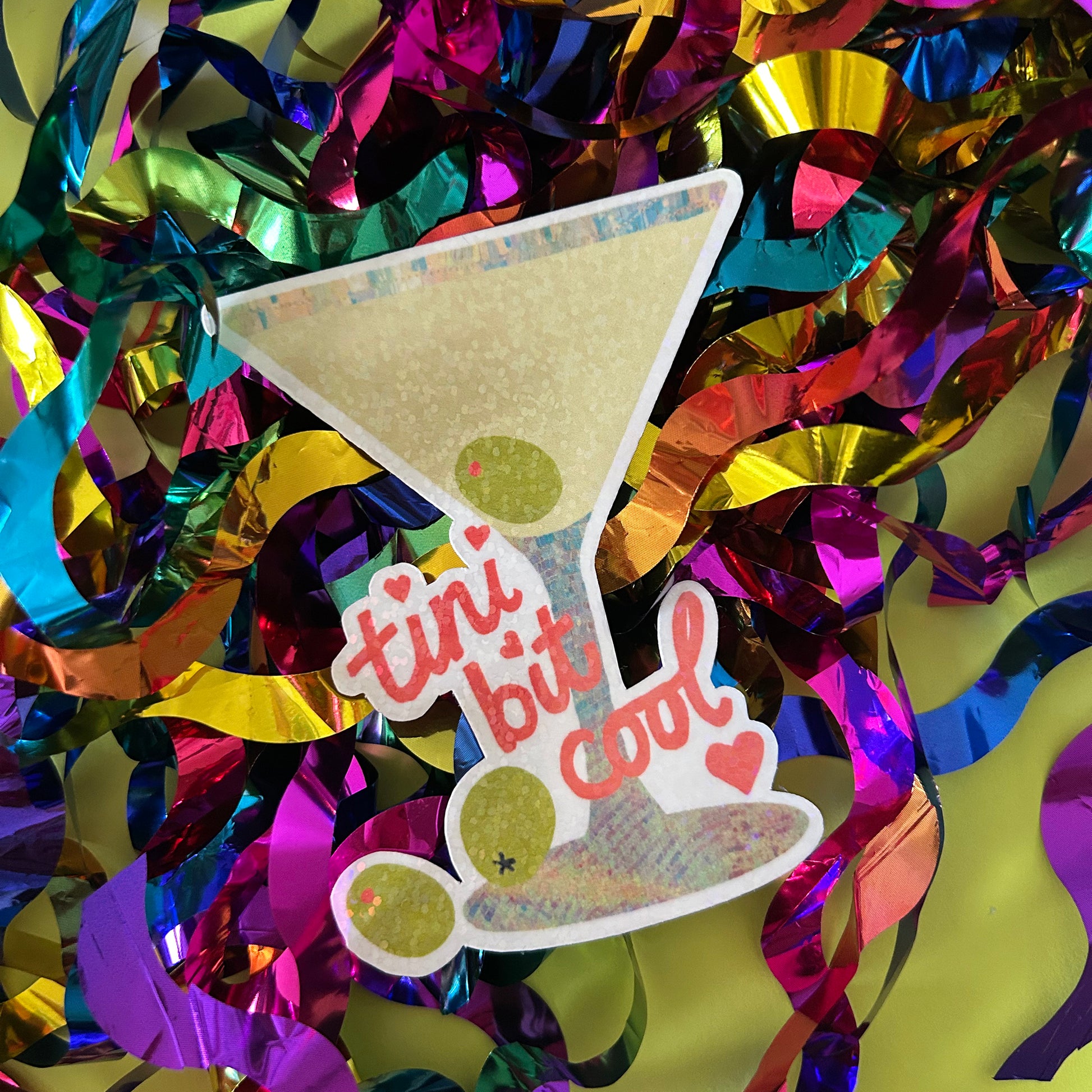 Colorful confetti with a cocktail glass-shaped sign saying 'tini bit cool' on a yellow background.