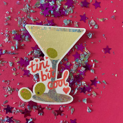 Sticker of a cocktail glass with 'tini bit cool' text on a pink background with star-shaped confetti.