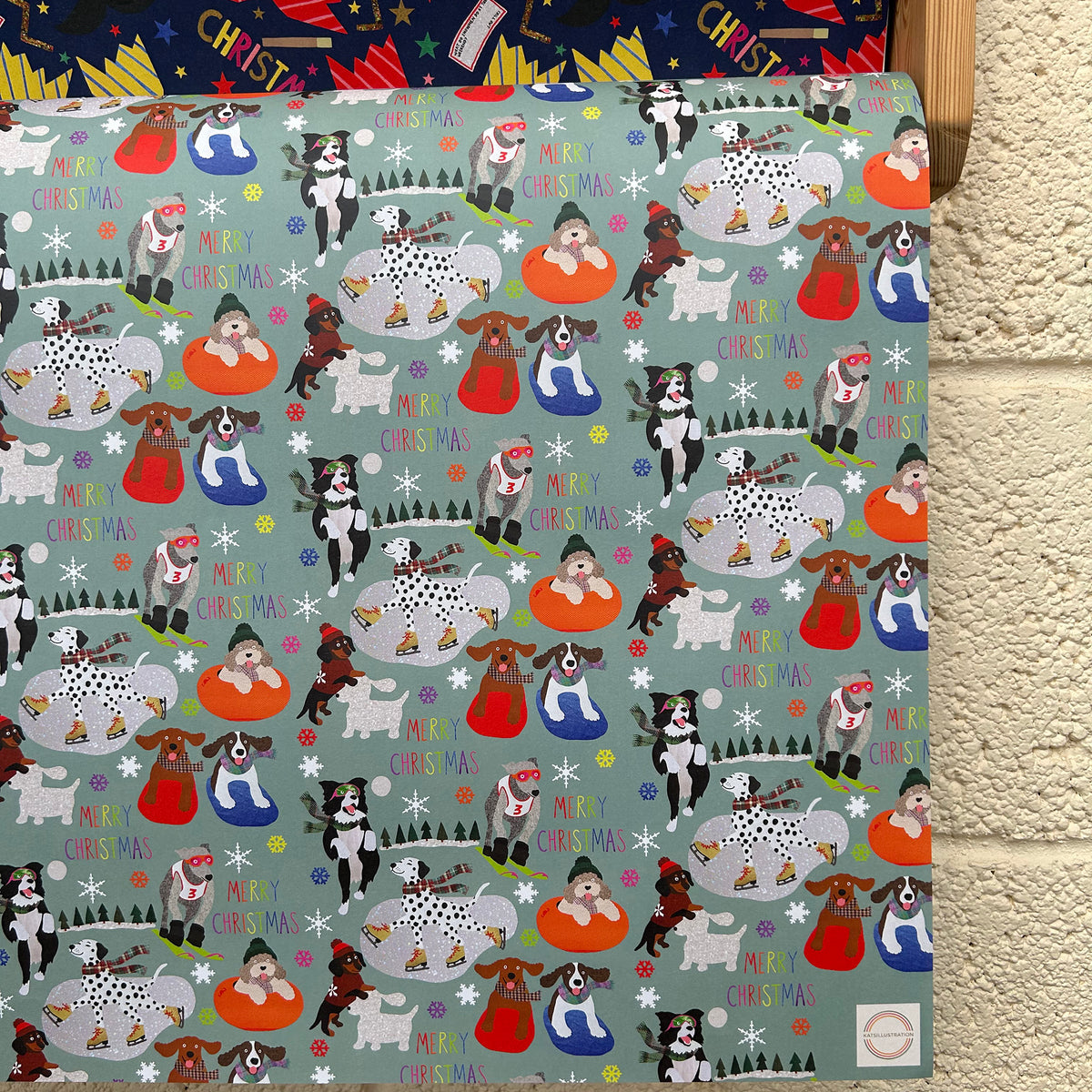 A festive Christmas gift wrap featuring a repeating pattern of dogs doing winter sports on a muted blue green background.