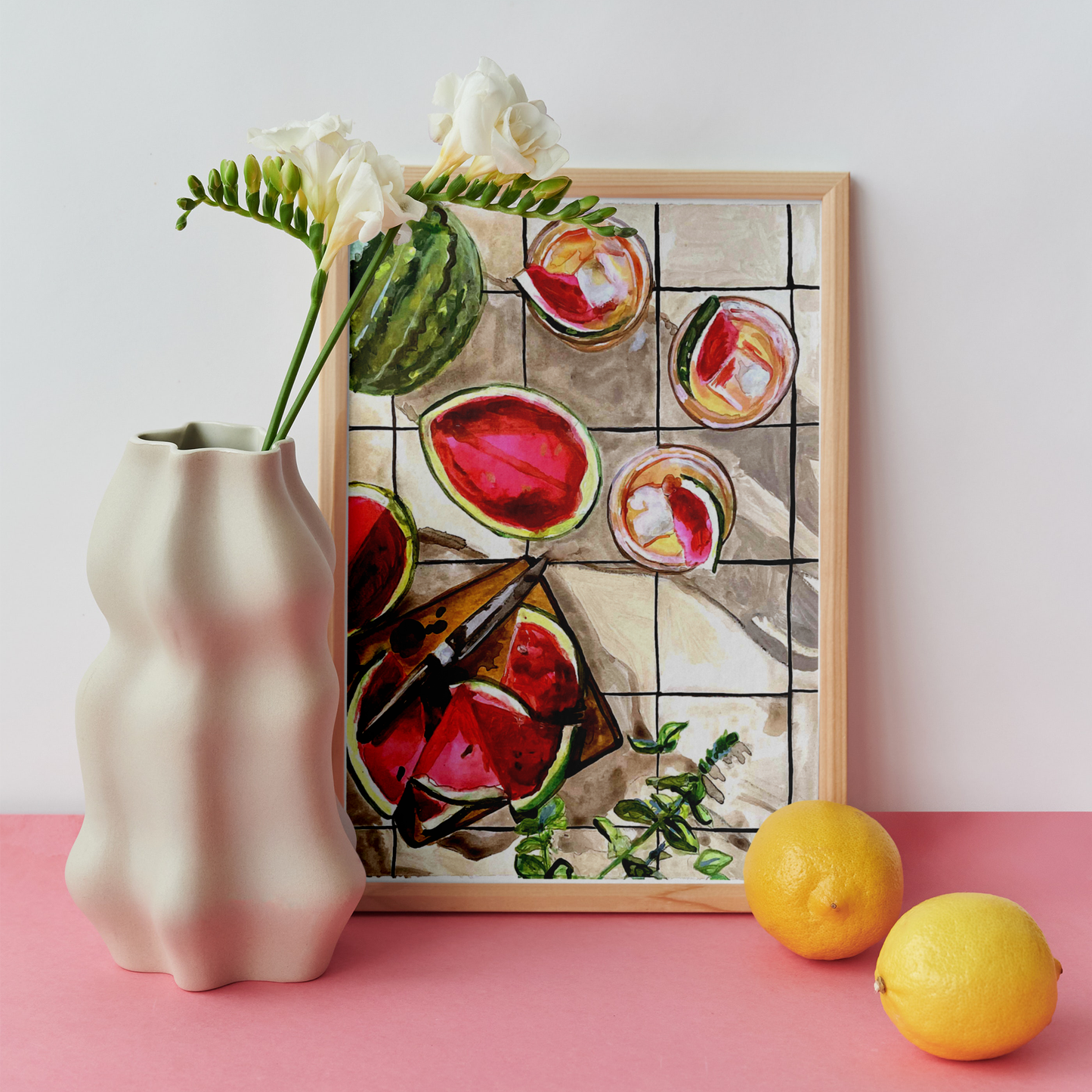 Framed artwork of watermelons on a pink surface with a vase and lemons.