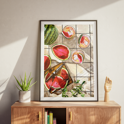 Framed artwork of watermelons on a wooden cabinet with a plant and sculpture.