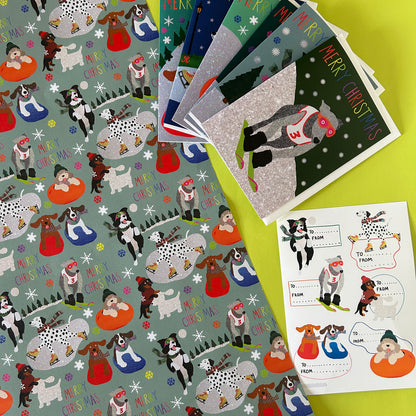 Christmas-themed dog gift set including patterned wrapping paper, greeting cards, and a sticker sheet on a bright yellow background.
