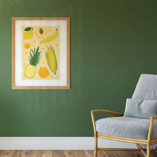 Image of a framed art print of yellow fruit and vegetables on a pale yellow background.