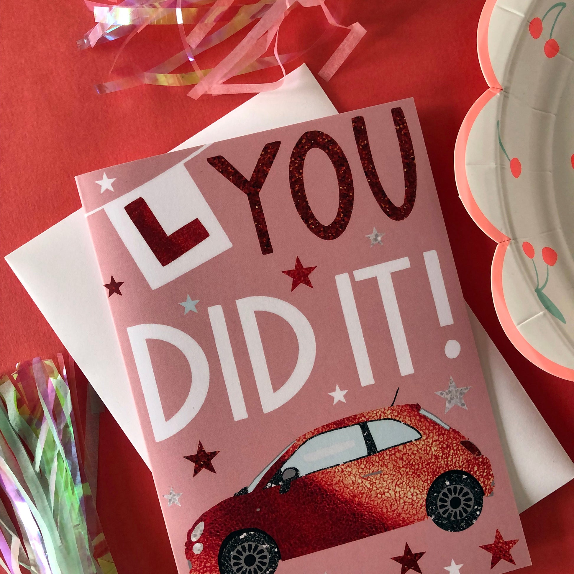 Image shows a pastel pink card with a red sparkly car and L Plate with the words "You Did It!'