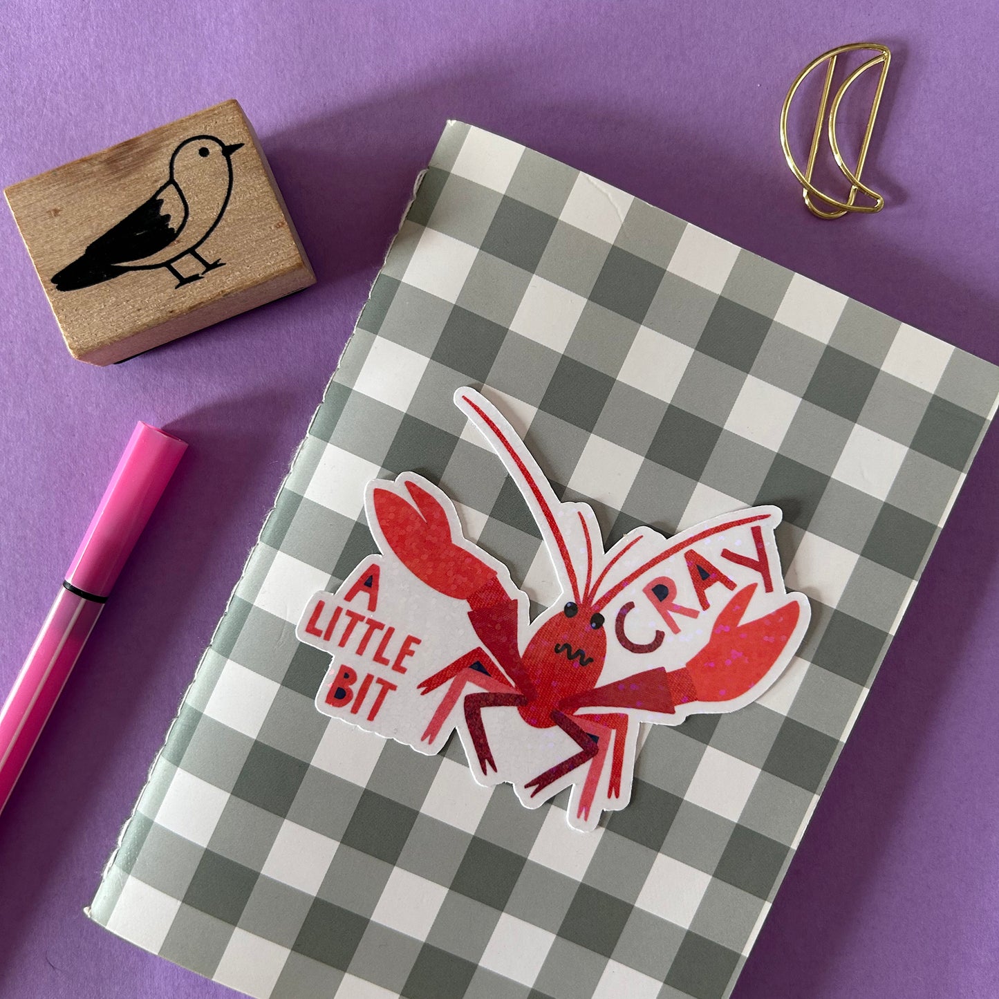 Checkered notebook with a red crayfish sticker on a purple background