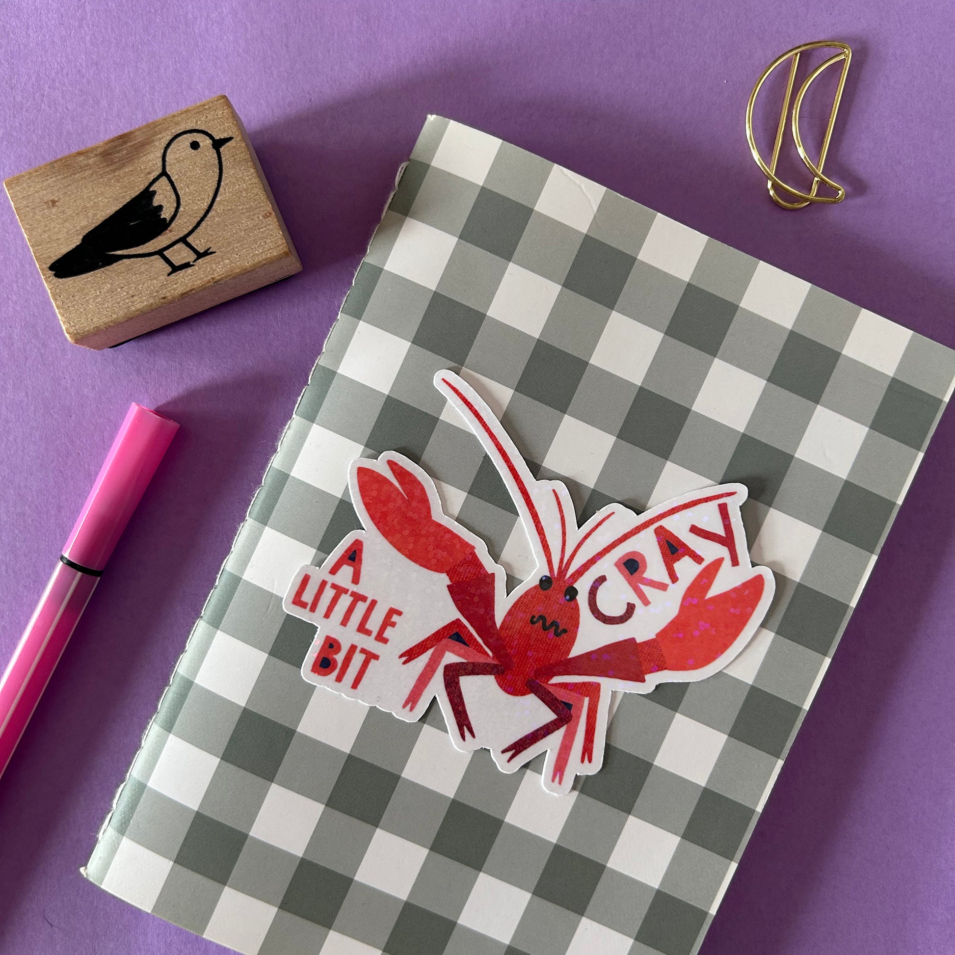 Checkered notebook with a red crayfish sticker on a purple background