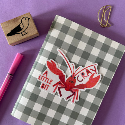 Checkered notebook with a red crayfish sticker on a purple background