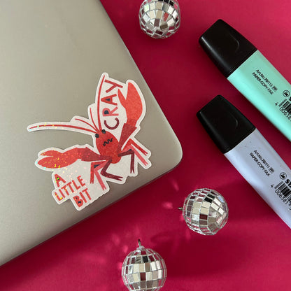 Sticker of a red crayfish with text on a laptop, surrounded by disco balls and markers.